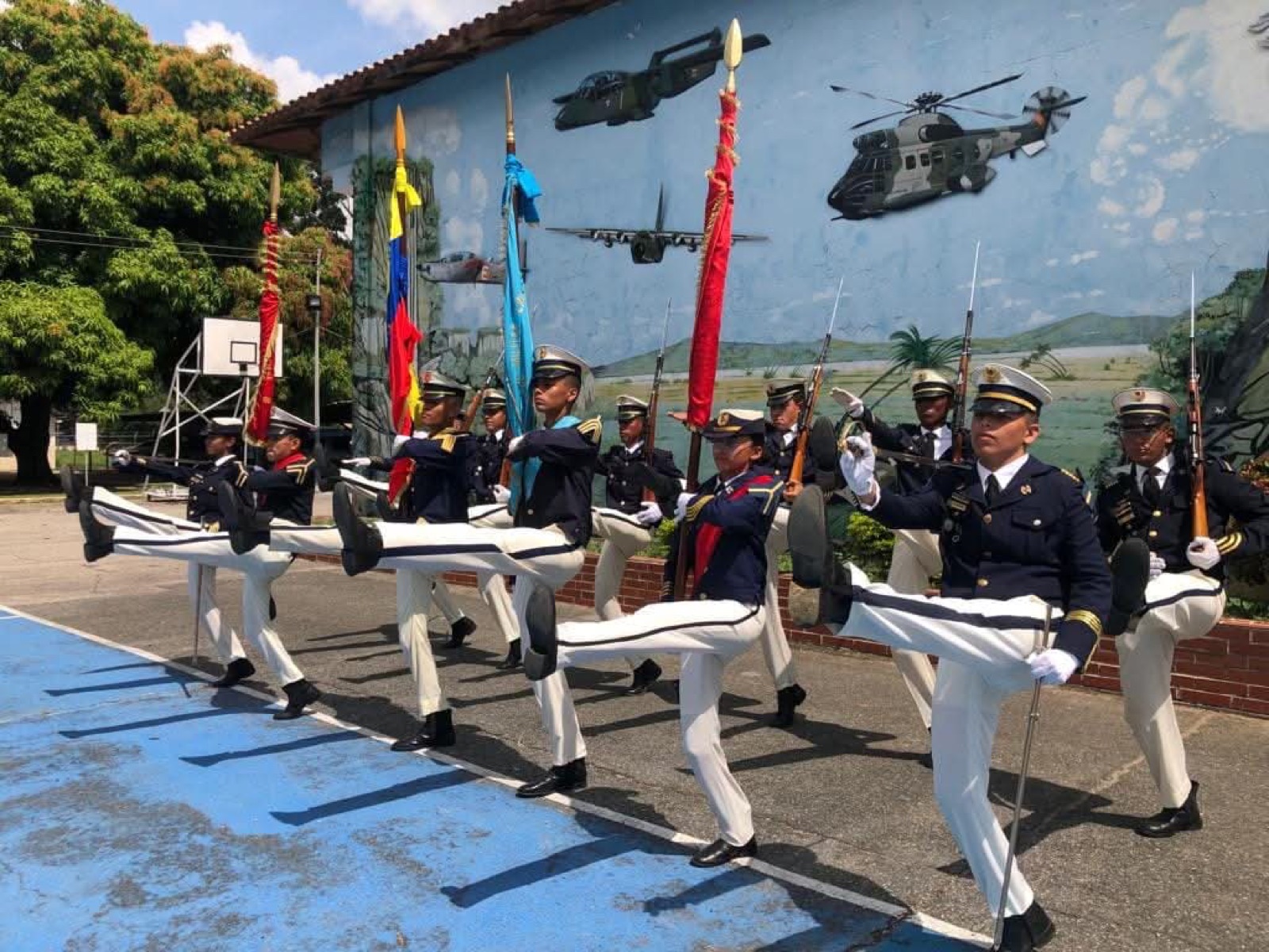 Escolta de bandera ejecutando el paso alto frente al mural de aeronaves del liceo